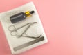 Nail saw, cuticle clippers, nail scissors and hand oil stand on a white towel that stands on a pink background. Top views