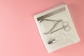 Nail saw, cuticle clippers, nail scissors and hand oil stand on a white towel that stands on a pink background. Top views