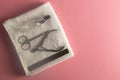 Nail saw, cuticle clippers, nail scissors and hand oil stand on a white towel that stands on a pink background. Top views