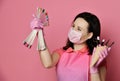 Master in pink gloves, apron and white mask holds manicure equipment in waffle cone and looks at nail varnish samples display