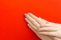 Nails Design. Hands With Bright Nude Manicure on red background. Top view