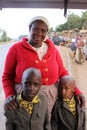 Black African old plump woman laughs merrily and holds the shoulders of two African boys embarrassed