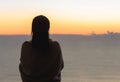 Naked beautiful female with wet hair wrapped in a blanket with cup of coffee standing on the glass balcony early morning at sunris