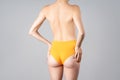 Naked female back, slim topless woman in yellow panties on gray background, body care and correction of scoliosis concept