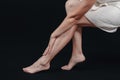 Naked long female legs. Female body in a towel. A woman is sitting on a stool, holding her leg. Foot massage. Side view Royalty Free Stock Photo