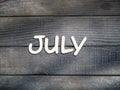 The name of the month is composed of light wooden letters on dark wood. The month of July.