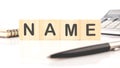 NAME word assembled from wooden cubes next to a calculator, pen and notepad
