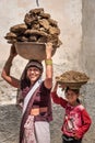 Indian woman and girl carrying basin with cow dung cakes on their heads in Nandgaon. India