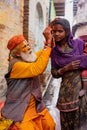 Elderly man paints symbols using gold paint onto the forehead of