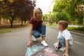 Nanny with cute little boy drawing  with chalks on asphalt Royalty Free Stock Photo