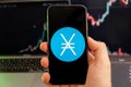 Nano XNO cryptocurrency logo on the screen of smartphone in mans hand with a growing trend on the chart on a green