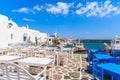 NAOUSSA PORT, PAROS ISLAND - MAY 20, 2016: Tavern tables and typical white Greek buildings in Naoussa port, Paros island, Cyclades Royalty Free Stock Photo