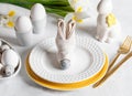 Napkin as bunny muzzle on plate, natural colors eggs, white Iris flowers, gold cutlery. White Easter