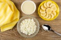 Napkin, bowl with condensed milk, cottage cheese in bowl, saucer with slices of banana, spoon on wooden table. Top view Royalty Free Stock Photo