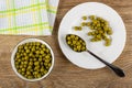 Napkin, bowl with green peas, spoon with green peas in plate on wooden table. Top view