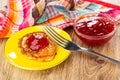 Napkin, bowl with jam, cheese pancake with strawberry jam in saucer, fork on wooden table