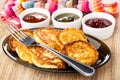 Napkin, bowls with jams, fried pancakes from cottage cheese in dish, fork on wooden table