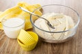 Napkin, cup of milk, silicone molds, flour mixture with butter for muffins, spoon in bowl, on wooden table