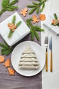 Napkin in the form of a Christmas tree on a plate on white tablecloth with gifts and decorations with fir sprigs and gingerbread Royalty Free Stock Photo