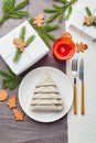 Napkin in the form of a Christmas tree on a plate on white tablecloth with gifts and decorations with fir sprigs and gingerbread Royalty Free Stock Photo