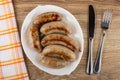 Napkin, fried chicken sausages on white dish, knife, fork on wooden table. Top view