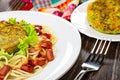 Napkin, vegetable cutlet with spaghetti and red beans in white dish, cutlets in plate, fork on wooden table