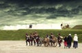 Napoleonic soldiers and women marching and pulling a cannon along a French camp with stormy clouds above. Soldiers