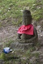 Traditional stone carved Jizo with red skirt honored and respected with a cup of water