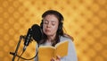 Narrator wearing headset reading aloud from book into mic, studio background