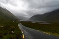 Narrow black-top highway leads through an overcast mountain valley with fog and mist and lakes o nthe valley bottom