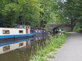 Boats and barges moored on the rochdale canal in hebden bridge bext to an old stone footbridge surrounded by green summer Royalty Free Stock Photo