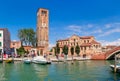 Narrow canal, church and tall belfry with clock in Murano.