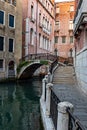Narrow canal with medieval buildings, stone walkway in Venice, Italy on sunny day
