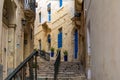 Narrow charming street in Birgu, Malta, with medieval buildings, blue doors and window shutters and plants pots