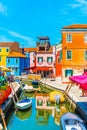 Narrow canal with blue, red, green and purple house facade in the island of Burano, Venice