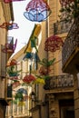 Narrow city street with wicker figures hanging between the roofs