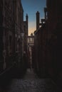 Narrow European alley, surrounded by bricks and cobblestone. Illuminated only with weak light from sunrise. Concept of Royalty Free Stock Photo