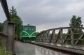 Narrow gauge green locomotive ride on bridge, rain weather. Czech republic