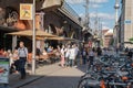 Narrow lane in city with cafes and people including group four young men in white tops with caps on backwards