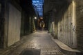 Narrow side street with closed white doors on each side and two dark human figures in the distance. Deserted urban road with stone Royalty Free Stock Photo