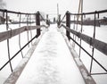 The narrow snow-covered bridge of metal and wood over frozen winter river in village.