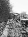 Narrow snow covered country road in rawtenstall near hebden bridge with stone wall and cottages in farmland with the pennine Royalty Free Stock Photo