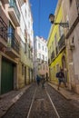 Narrow street in old town of Lisbon, Portugal. Tourists in historical district of Lisboa. Colorful cityscape at sunny summer day. Royalty Free Stock Photo