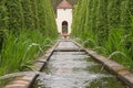 Narrow water canal with thin fountains directed to a park entrance