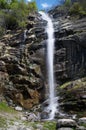 Narrow white stream of water flows over a wet stone cliff