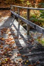 Narrow wooden footbridge with fallen leaves over a river in an autumn maple forest lit by the sun in Vermont Royalty Free Stock Photo