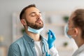 Nasal coronavirus PCR test. Doctor using swab stick to take covid virus specimen from potentially infected young guy Royalty Free Stock Photo