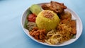 Nasi Kuning or Yellow rice with traditional fried chicken, tofu, tempeh, and smashed potato on blue background. Royalty Free Stock Photo