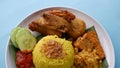 Nasi Kuning or Yellow rice with traditional fried chicken, tofu, tempeh, and smashed potato on blue background. Royalty Free Stock Photo