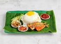 nasi lemak set with sunny egg, rice, fried fish, pickle, salad, peanut and chilli sauce served in dish isolated on banana leaf top Royalty Free Stock Photo